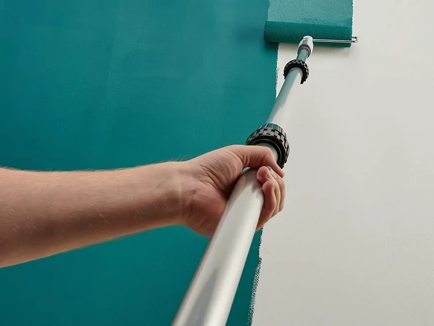 Painting a wall with a roller mounted on an extension pole