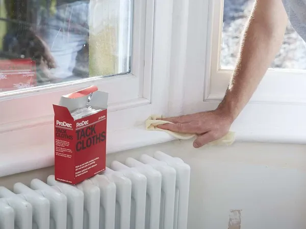 Wiping a window sill with a tack cloth to remove dust